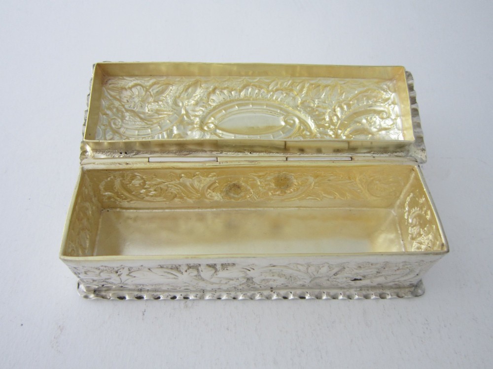 A small rectangular sterling silver trinket box decorated with detailed repousse floral scrollwork and crimped borders. View III