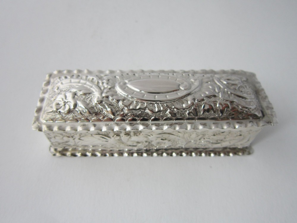 A small rectangular sterling silver trinket box decorated with detailed repousse floral scrollwork and crimped borders. View IV