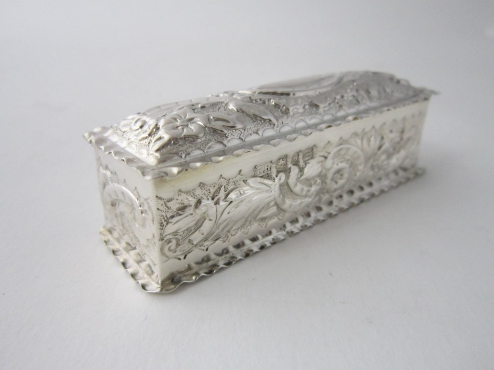 A small rectangular sterling silver trinket box decorated with detailed repousse floral scrollwork and crimped borders. View V