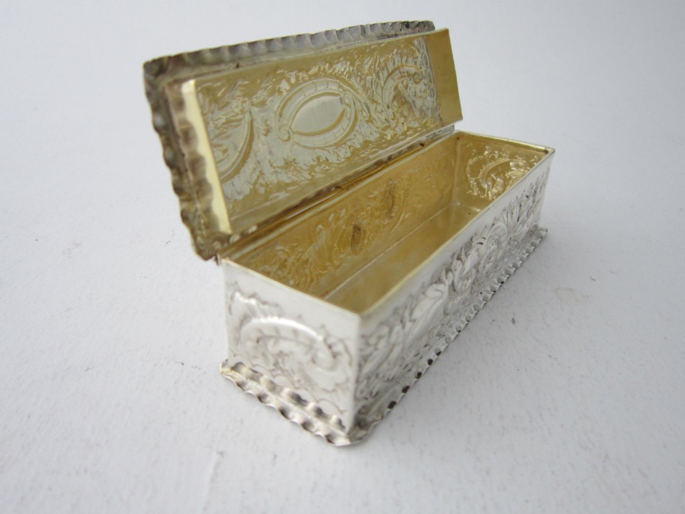 A small rectangular sterling silver trinket box decorated with detailed repousse floral scrollwork and crimped borders. View VII