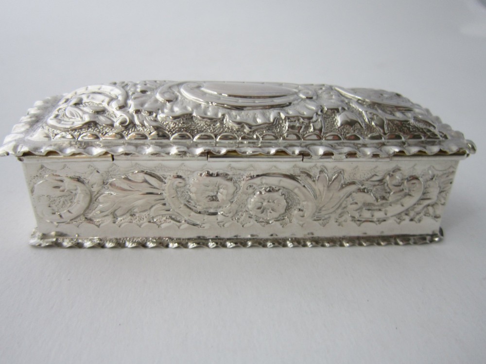 A small rectangular sterling silver trinket box decorated with detailed repousse floral scrollwork and crimped borders. View VIII