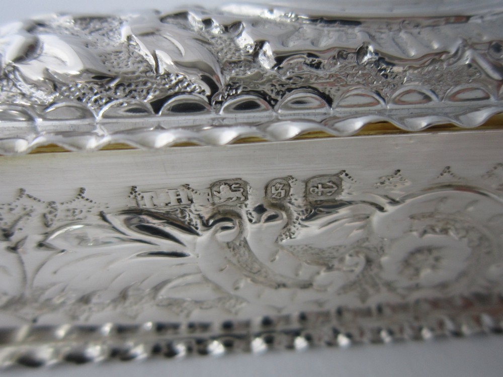 A small rectangular sterling silver trinket box decorated with detailed repousse floral scrollwork and crimped borders. View IX