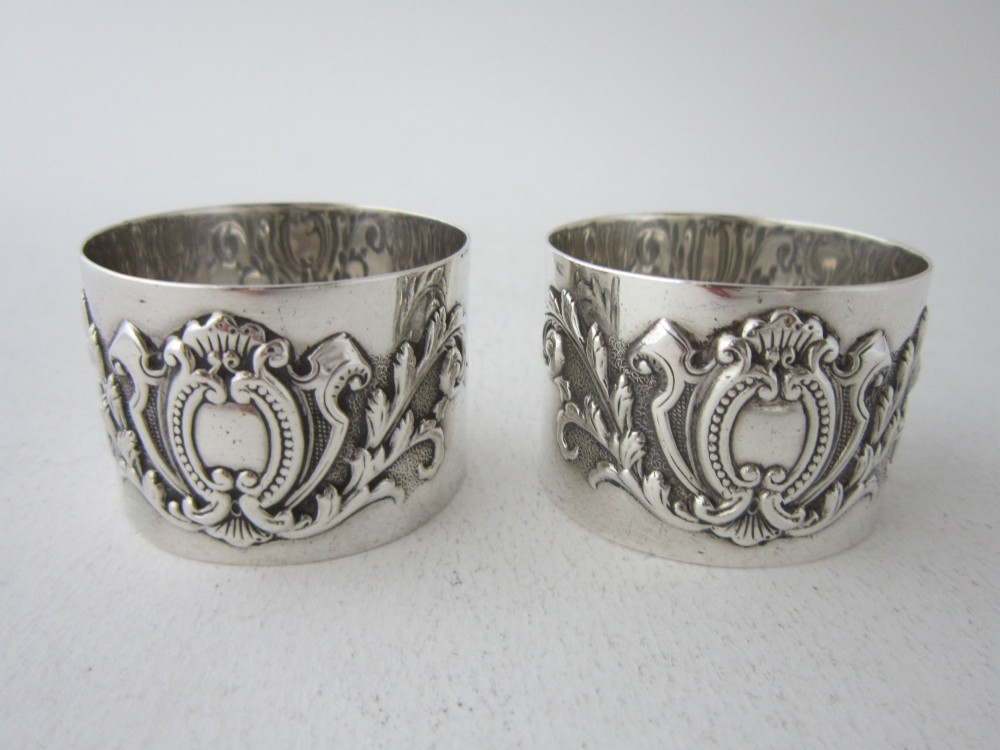 A pair of ornate Victorian sterling silver napkin rings featuring embossed acanthus leaves and cartouches inside a velvet-lined black presentation box. View III