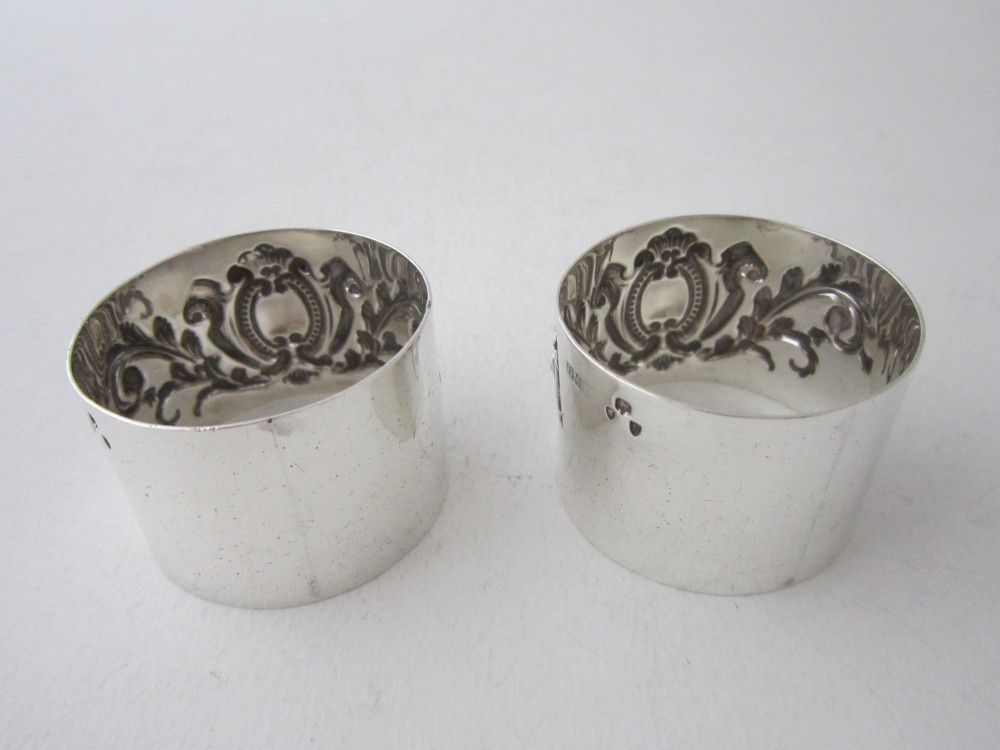 A pair of ornate Victorian sterling silver napkin rings featuring embossed acanthus leaves and cartouches inside a velvet-lined black presentation box. View IV
