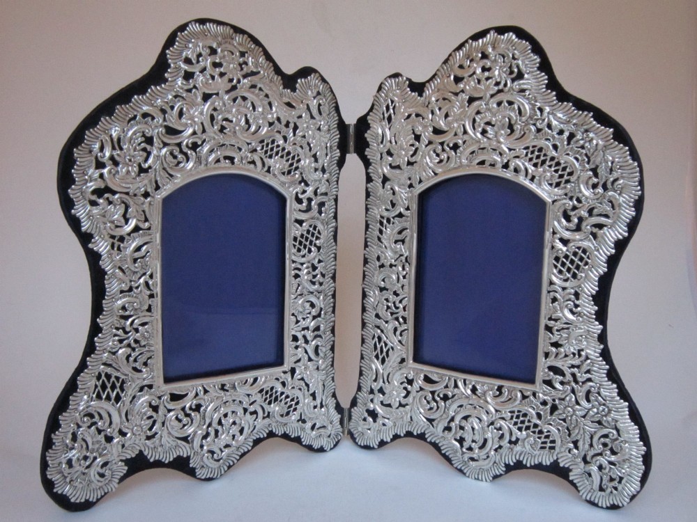An antique Victorian double sterling silver photograph frame featuring intricate pierced repousse scrollwork and dark velvet backing.