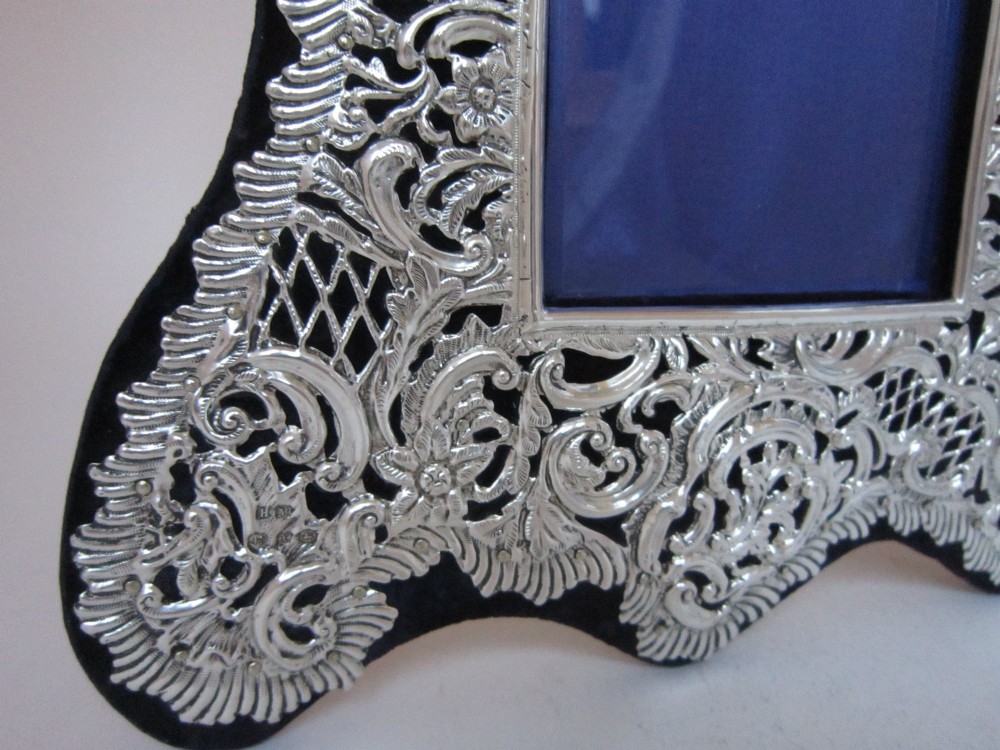 An antique Victorian double sterling silver photograph frame featuring intricate pierced repousse scrollwork and dark velvet backing. View IV