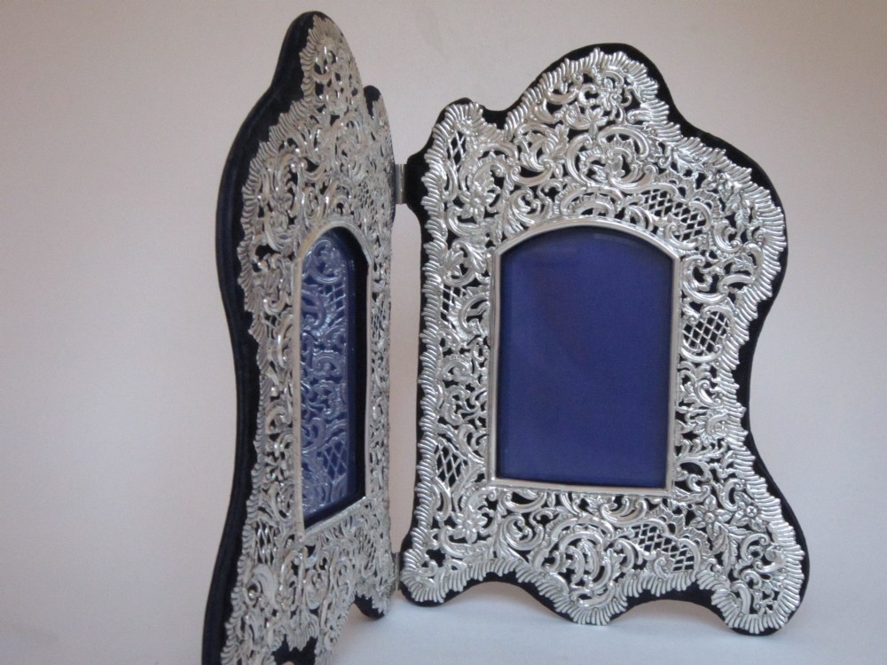 An antique Victorian double sterling silver photograph frame featuring intricate pierced repousse scrollwork and dark velvet backing. View VI
