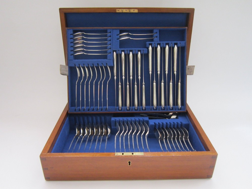 An open wooden canteen box lined with blue fabric displaying a complete set of Victorian sterling silver fiddle pattern cutlery.