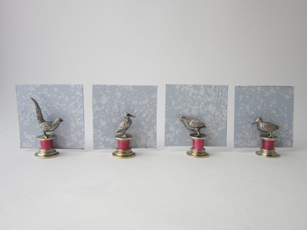 A set of four Edwardian sterling silver place card holders featuring pink guilloche enamel columns topped with sculpted game birds inside a fitted presentation box. View XIII