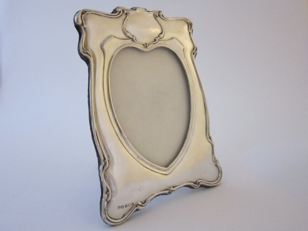 An Edwardian sterling silver photograph frame featuring sinuous Art Nouveau scrolls, a heart-shaped central aperture, and visible British hallmarks.