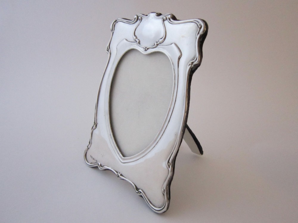 An Edwardian sterling silver photograph frame featuring sinuous Art Nouveau scrolls, a heart-shaped central aperture, and visible British hallmarks. View II