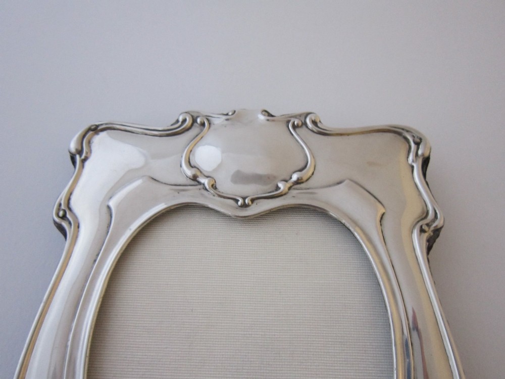 An Edwardian sterling silver photograph frame featuring sinuous Art Nouveau scrolls, a heart-shaped central aperture, and visible British hallmarks. View VI
