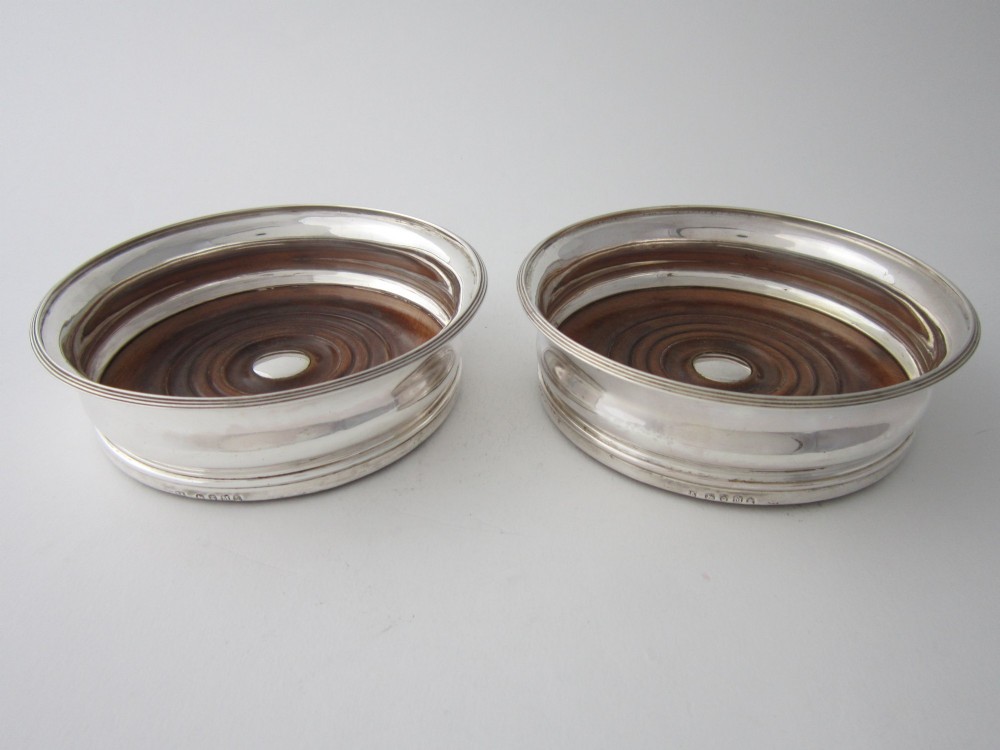 A pair of circular George III sterling silver wine coasters featuring turned wooden bases with central silver bosses and plain silver rims.