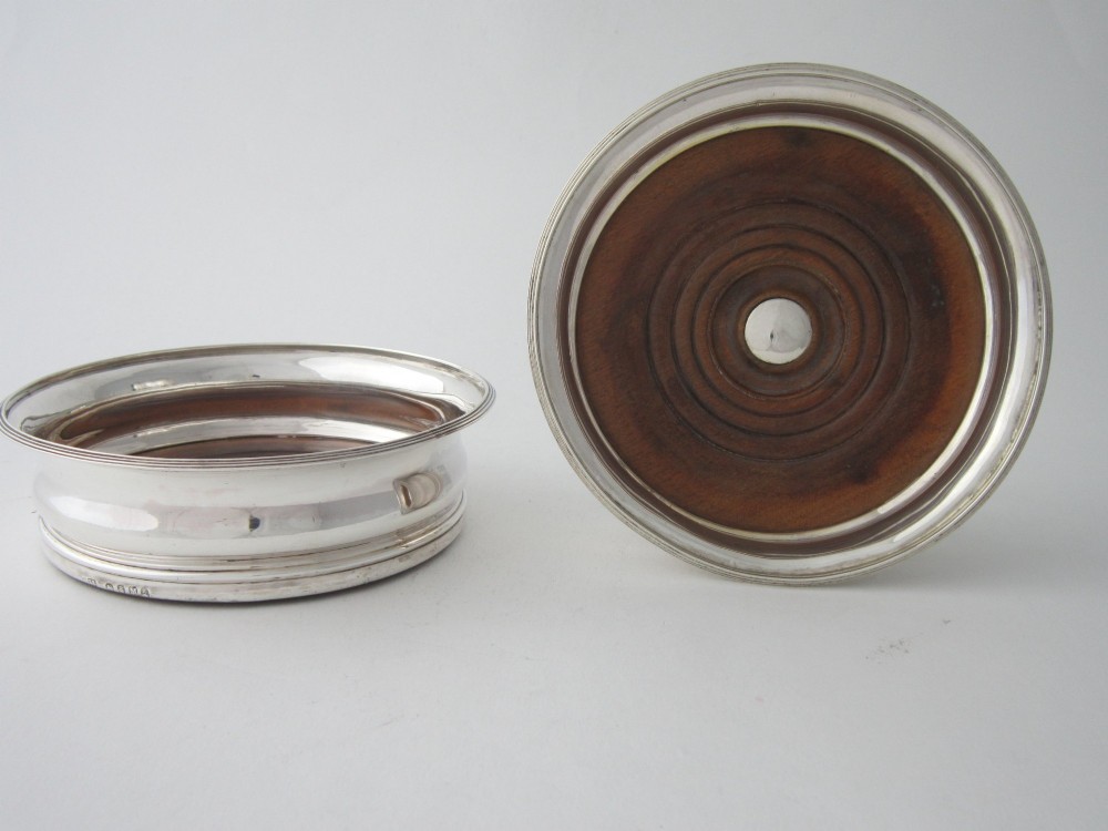 A pair of circular George III sterling silver wine coasters featuring turned wooden bases with central silver bosses and plain silver rims. View III