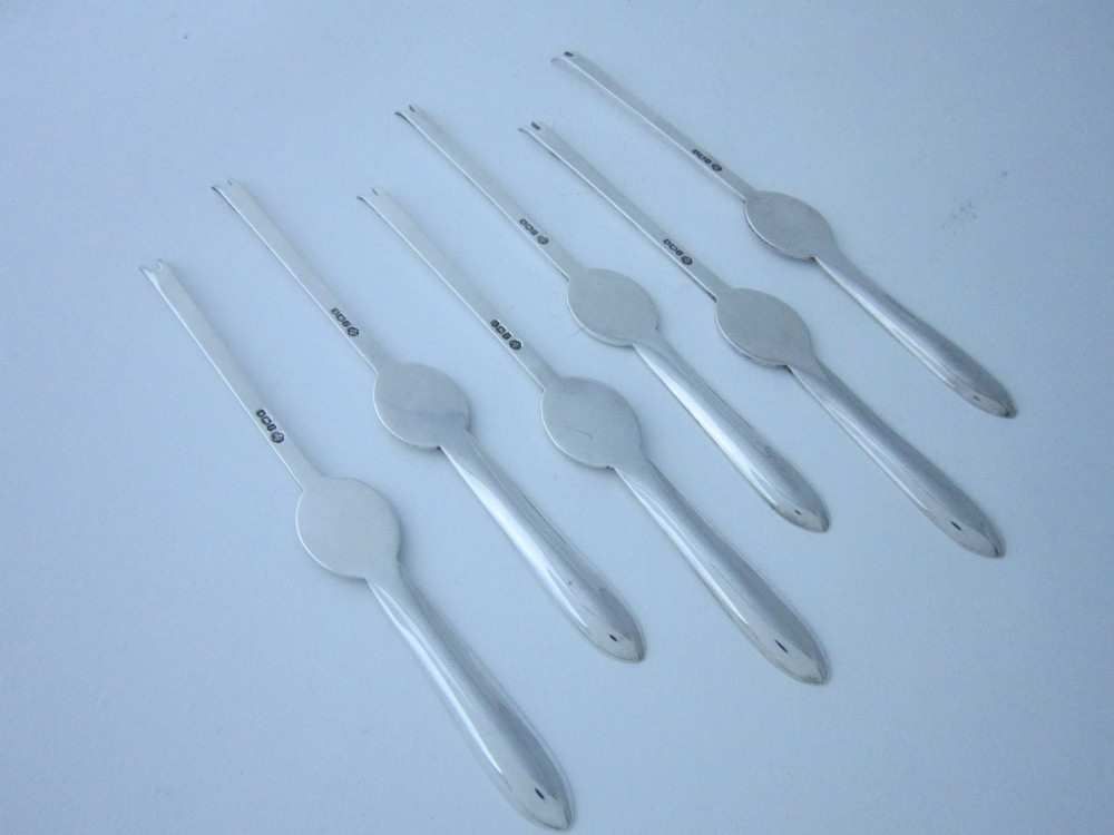 A set of six George V sterling silver lobster picks featuring central embossed lobster medallions, presented inside an open navy blue fitted velvet display case. View VII