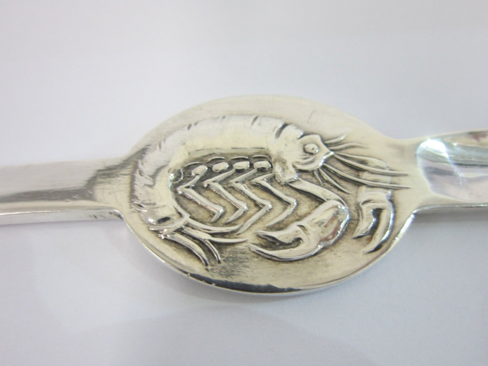A set of six George V sterling silver lobster picks featuring central embossed lobster medallions, presented inside an open navy blue fitted velvet display case. View X