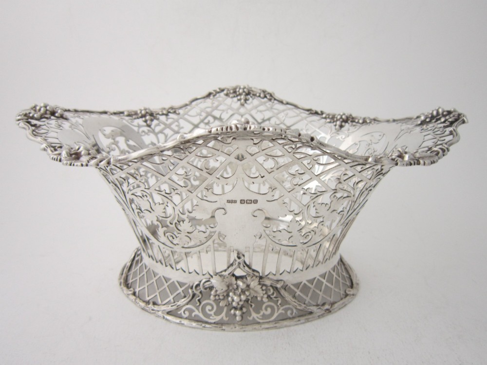 An antique George V sterling silver basket featuring intricate pierced lattice metalwork, scrolled grapevine borders, and visible hallmarks.