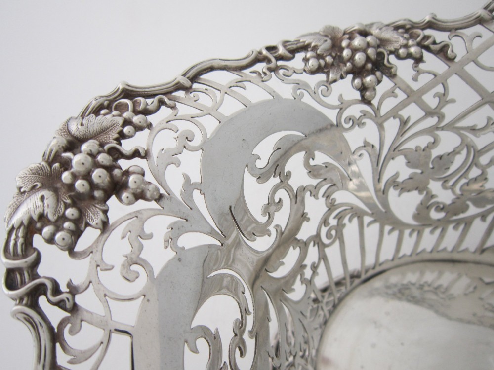 An antique George V sterling silver basket featuring intricate pierced lattice metalwork, scrolled grapevine borders, and visible hallmarks. View V