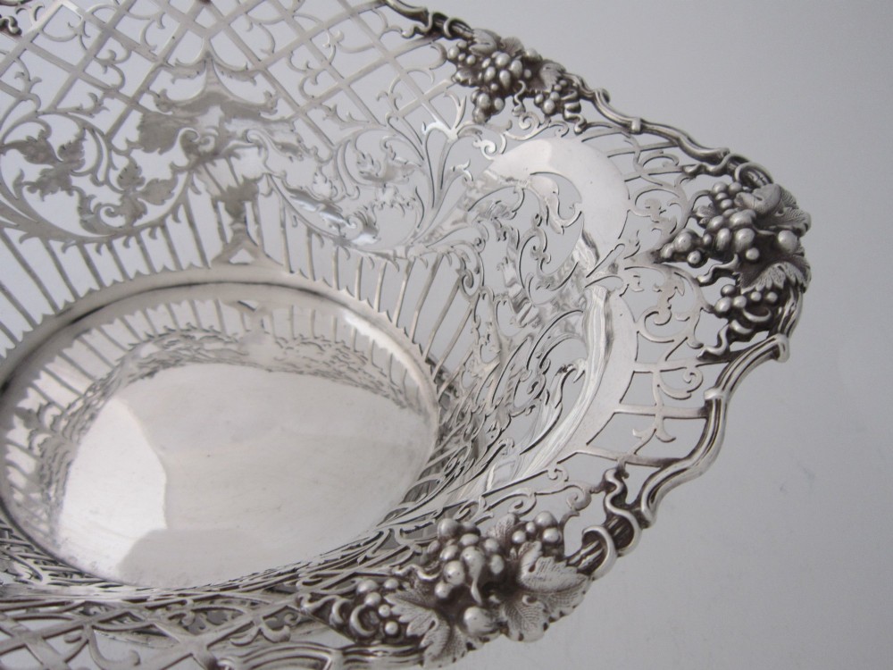 An antique George V sterling silver basket featuring intricate pierced lattice metalwork, scrolled grapevine borders, and visible hallmarks. View VI