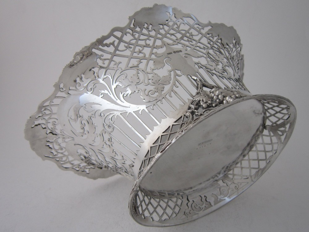 An antique George V sterling silver basket featuring intricate pierced lattice metalwork, scrolled grapevine borders, and visible hallmarks. View VIII