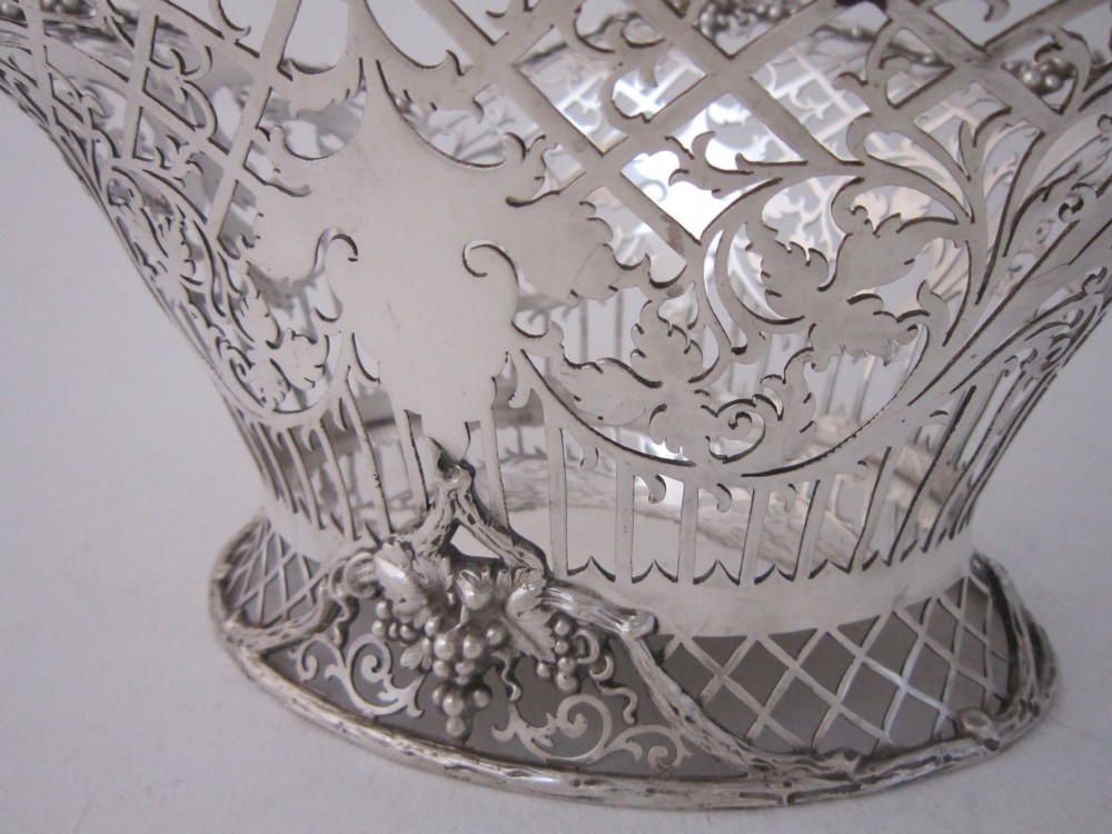 An antique George V sterling silver basket featuring intricate pierced lattice metalwork, scrolled grapevine borders, and visible hallmarks. View X