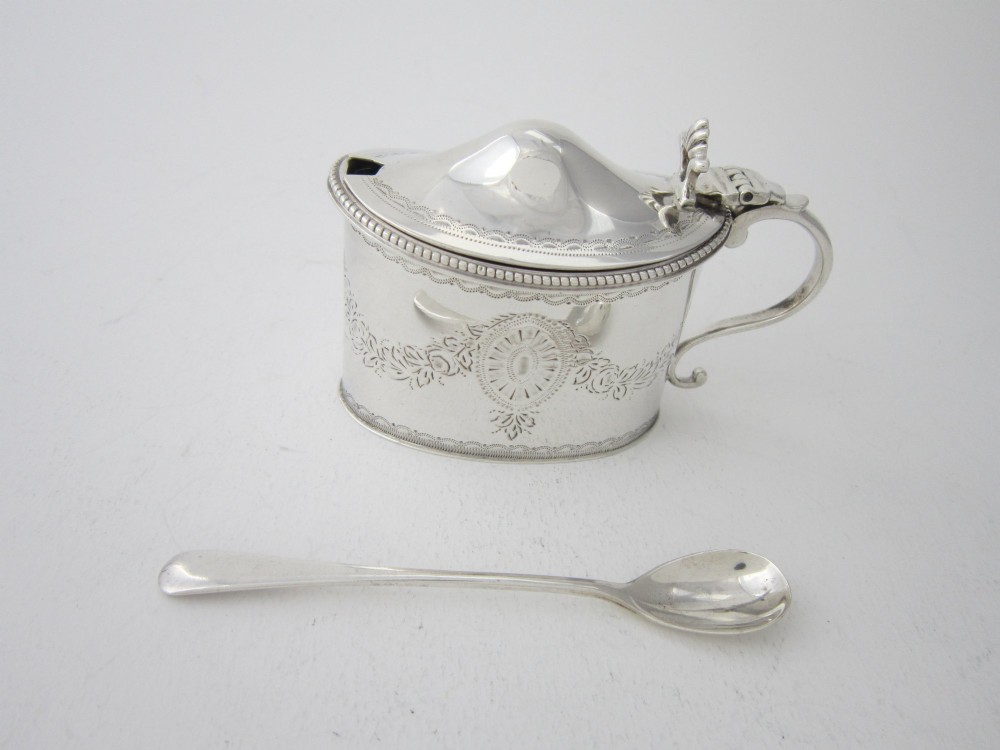 An oval sterling silver mustard pot featuring bright-cut engraved patterns, a beaded rim, a scroll handle, and a matching spoon. View II