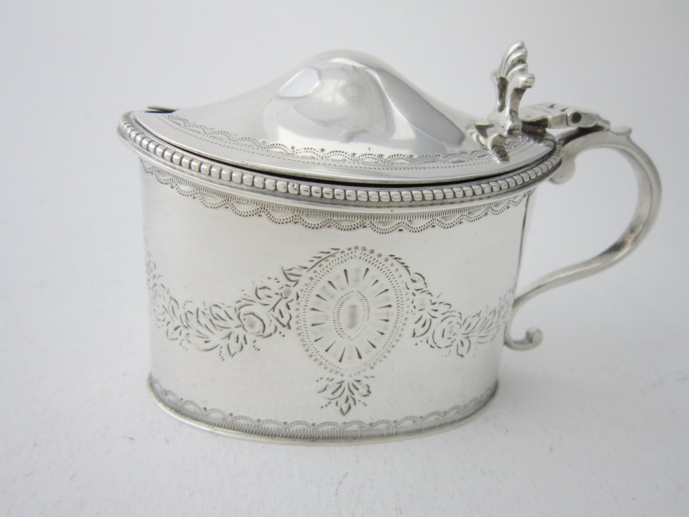 An oval sterling silver mustard pot featuring bright-cut engraved patterns, a beaded rim, a scroll handle, and a matching spoon. View III
