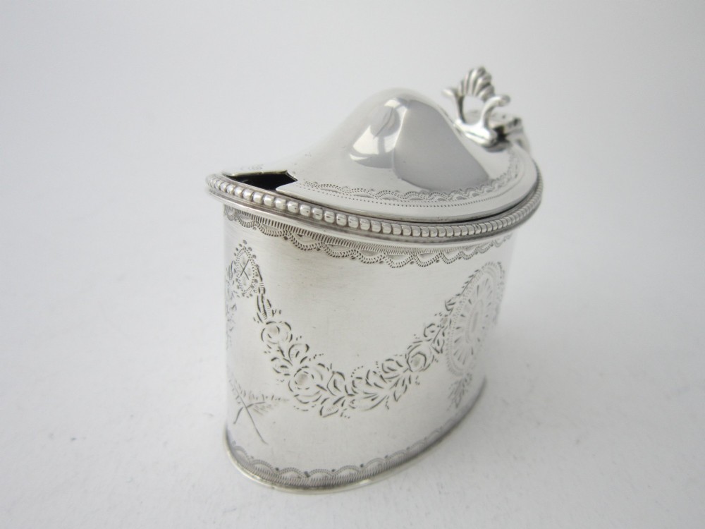 An oval sterling silver mustard pot featuring bright-cut engraved patterns, a beaded rim, a scroll handle, and a matching spoon. View IV