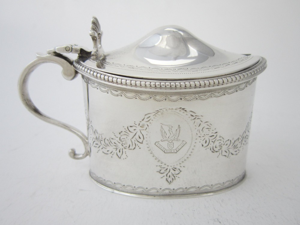 An oval sterling silver mustard pot featuring bright-cut engraved patterns, a beaded rim, a scroll handle, and a matching spoon. View V