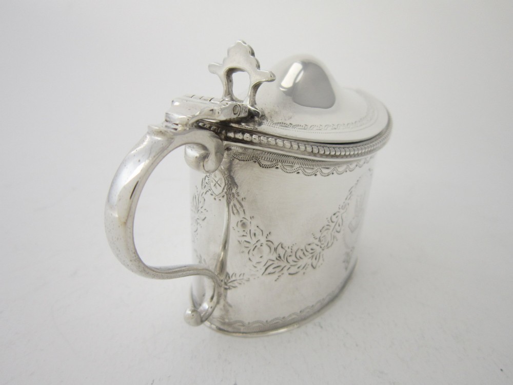 An oval sterling silver mustard pot featuring bright-cut engraved patterns, a beaded rim, a scroll handle, and a matching spoon. View VI