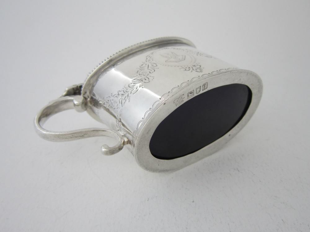 An oval sterling silver mustard pot featuring bright-cut engraved patterns, a beaded rim, a scroll handle, and a matching spoon. View IX