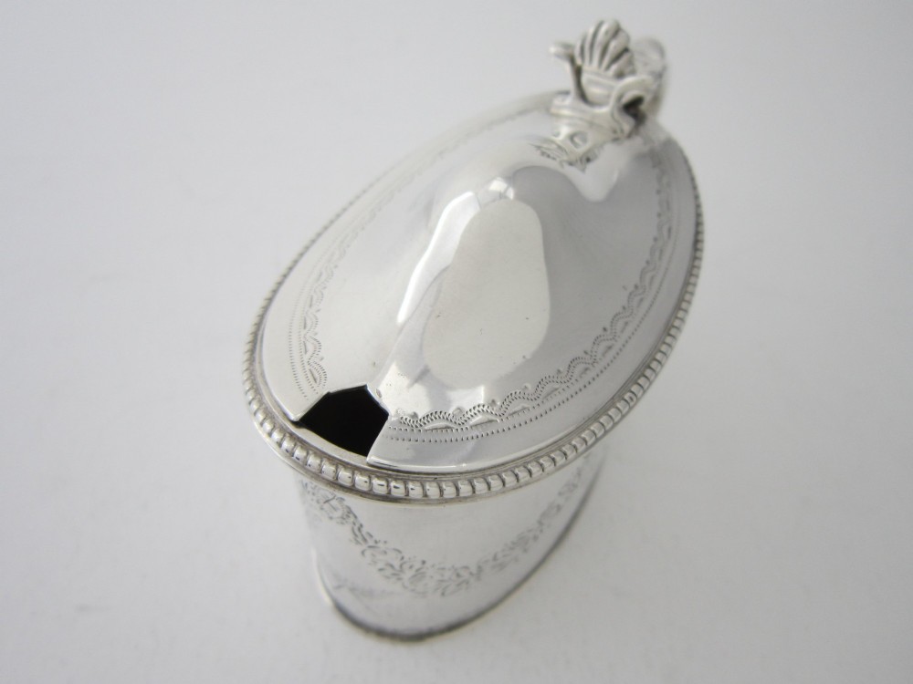 An oval sterling silver mustard pot featuring bright-cut engraved patterns, a beaded rim, a scroll handle, and a matching spoon. View XI