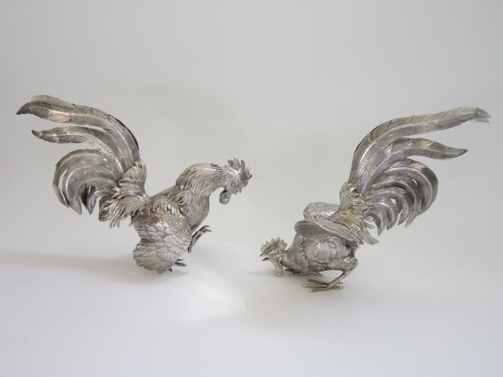 A pair of detailed sterling silver figures depicting fighting cockerels with open wings and realistic feather textures.