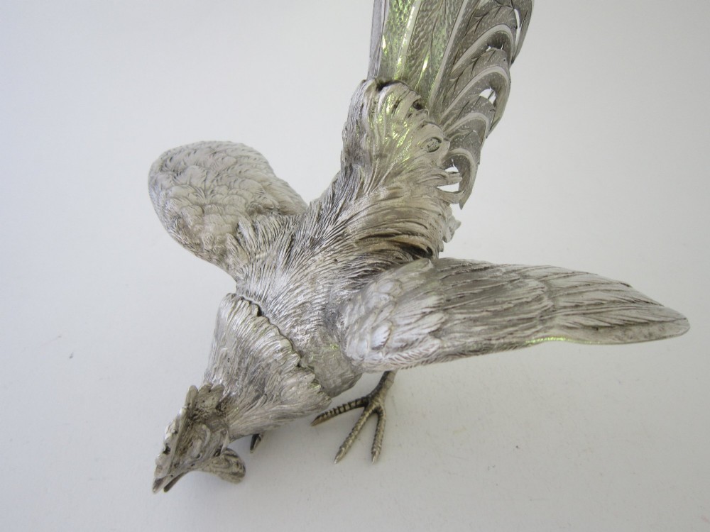 A pair of detailed sterling silver figures depicting fighting cockerels with open wings and realistic feather textures. View V