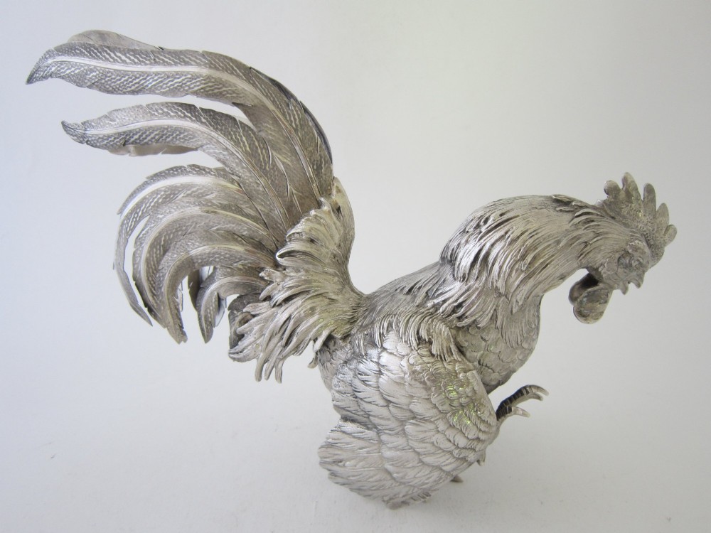 A pair of detailed sterling silver figures depicting fighting cockerels with open wings and realistic feather textures. View X