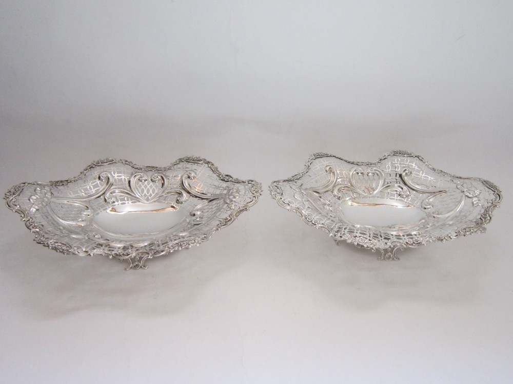 A pair of late Victorian sterling silver dishes featuring intricate pierced lattice pattern, ornate scroll borders, and raised feet.
