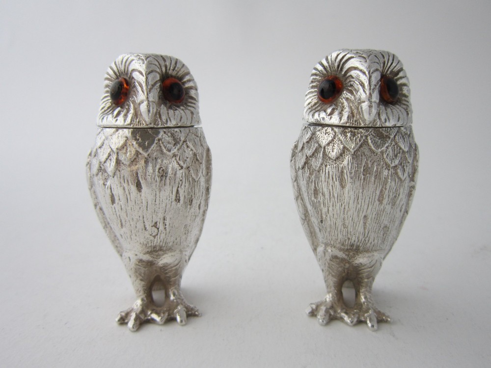 A pair of cast sterling silver salt and pepper shakers in the form of standing owls with textured feather detailing and dark amber glass eyes.