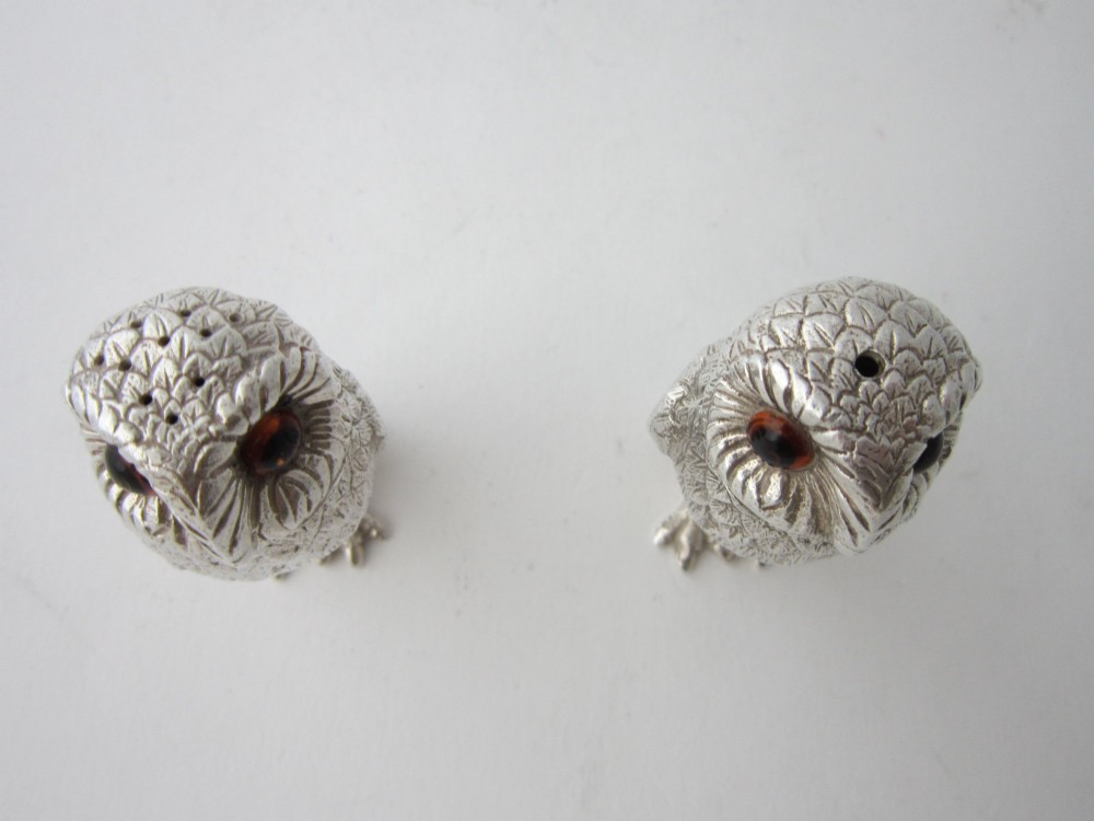 A pair of cast sterling silver salt and pepper shakers in the form of standing owls with textured feather detailing and dark amber glass eyes. View V