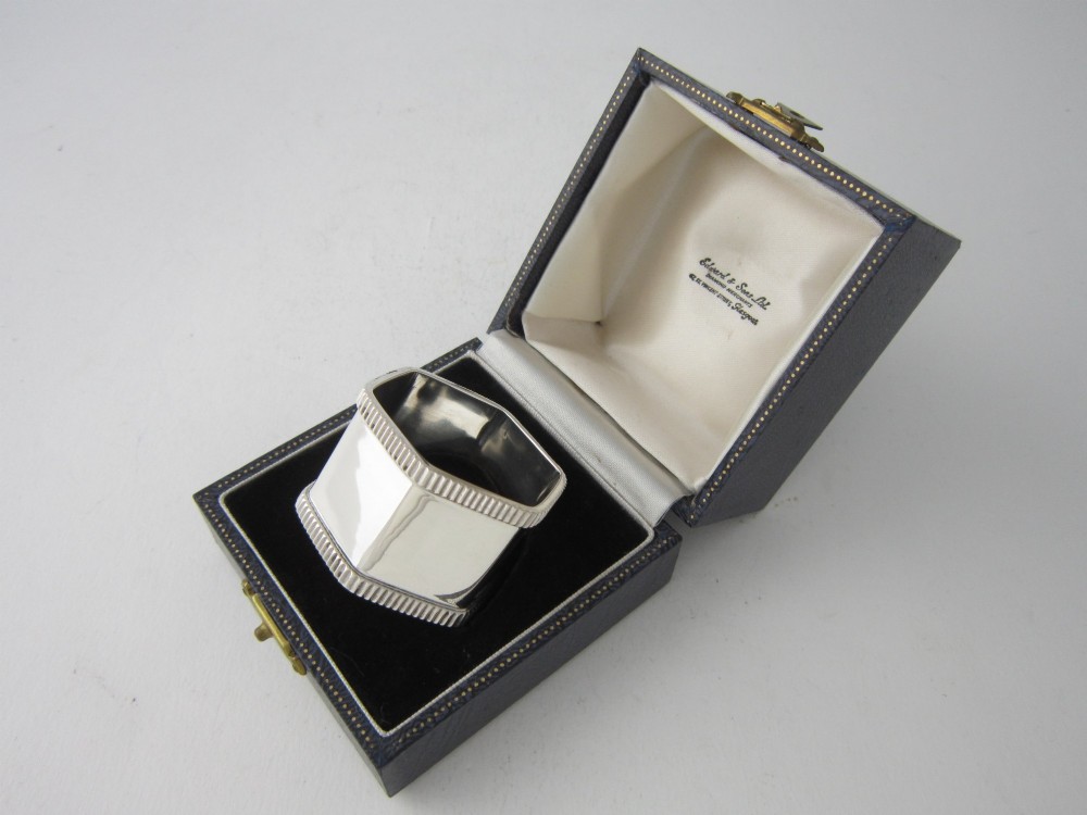 An octagonal sterling silver napkin ring with reeded borders presented inside a fitted blue velvet case.