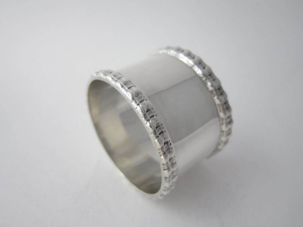An Edwardian sterling silver napkin ring featuring embossed patterned borders along the top and bottom rims. View II