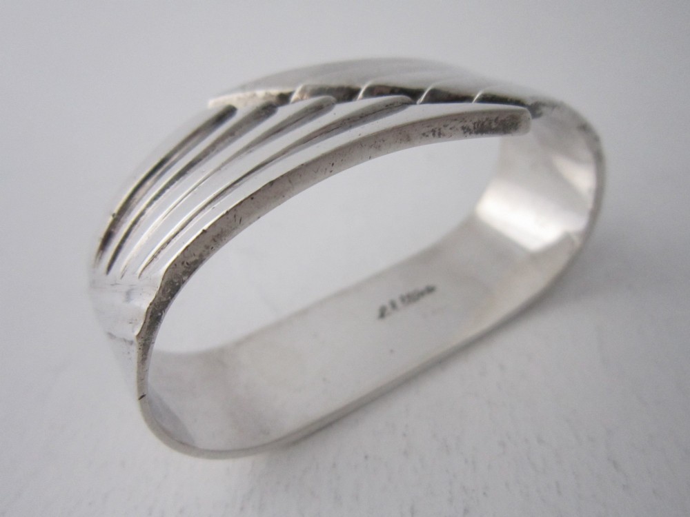 A sterling silver napkin ring crafted in 1949 with an asymmetrical geometric motif featuring grooved stepped lines. View II