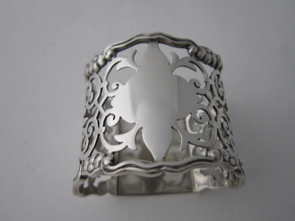 An antique George V sterling silver napkin ring featuring intricate pierced scrollwork and a blank central cartouche.