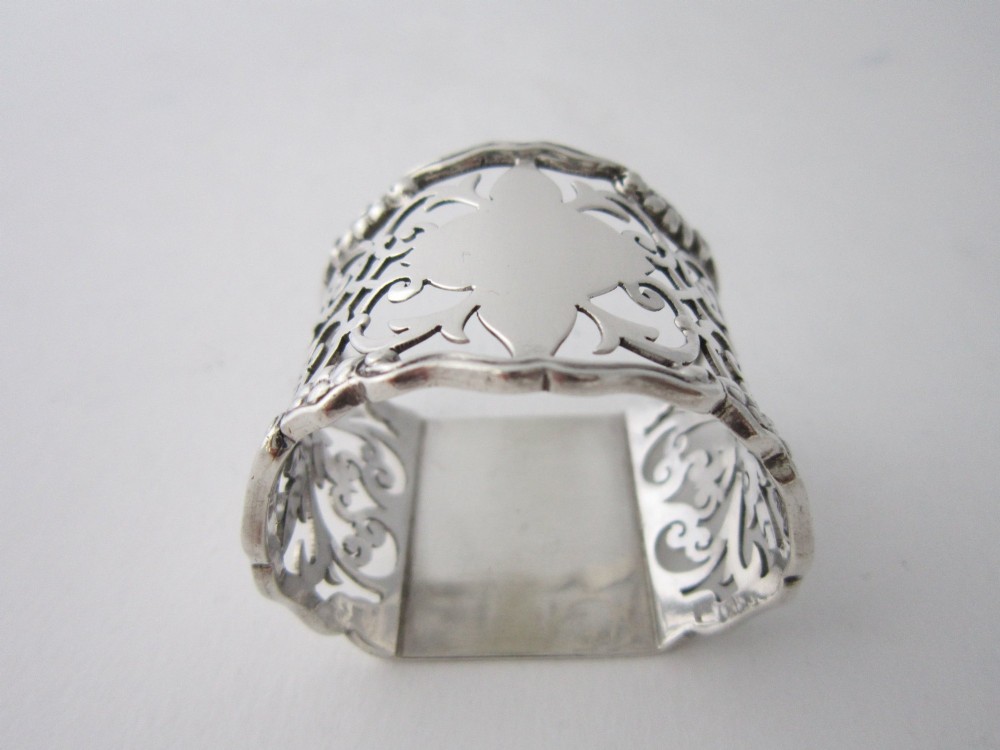 An antique George V sterling silver napkin ring featuring intricate pierced scrollwork and a blank central cartouche. View II