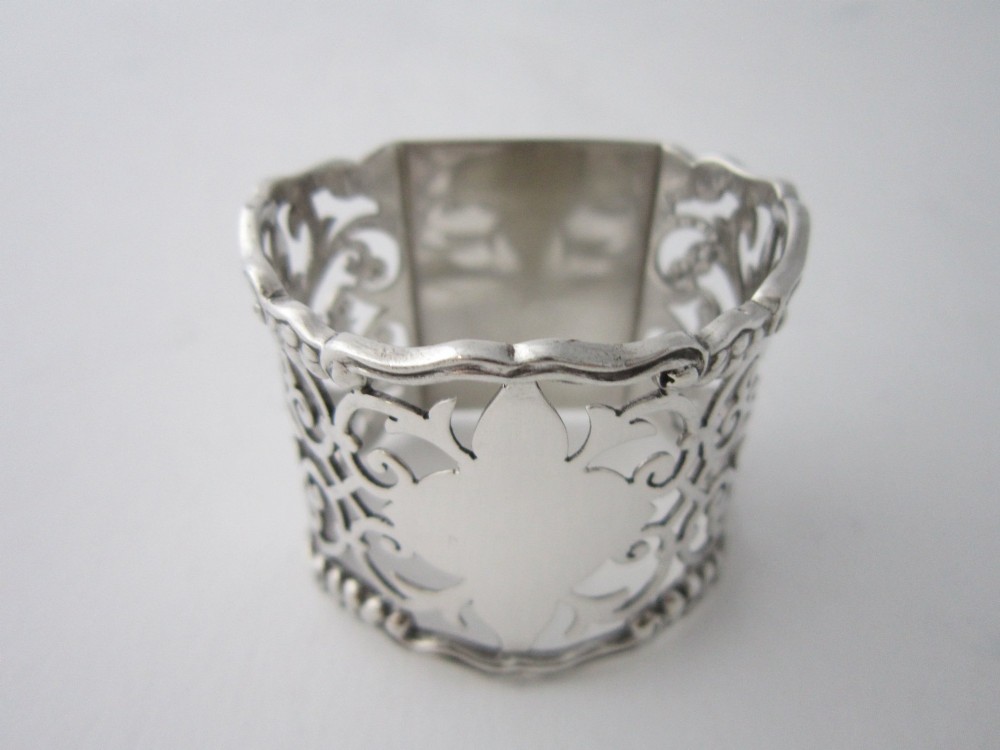 An antique George V sterling silver napkin ring featuring intricate pierced scrollwork and a blank central cartouche. View III