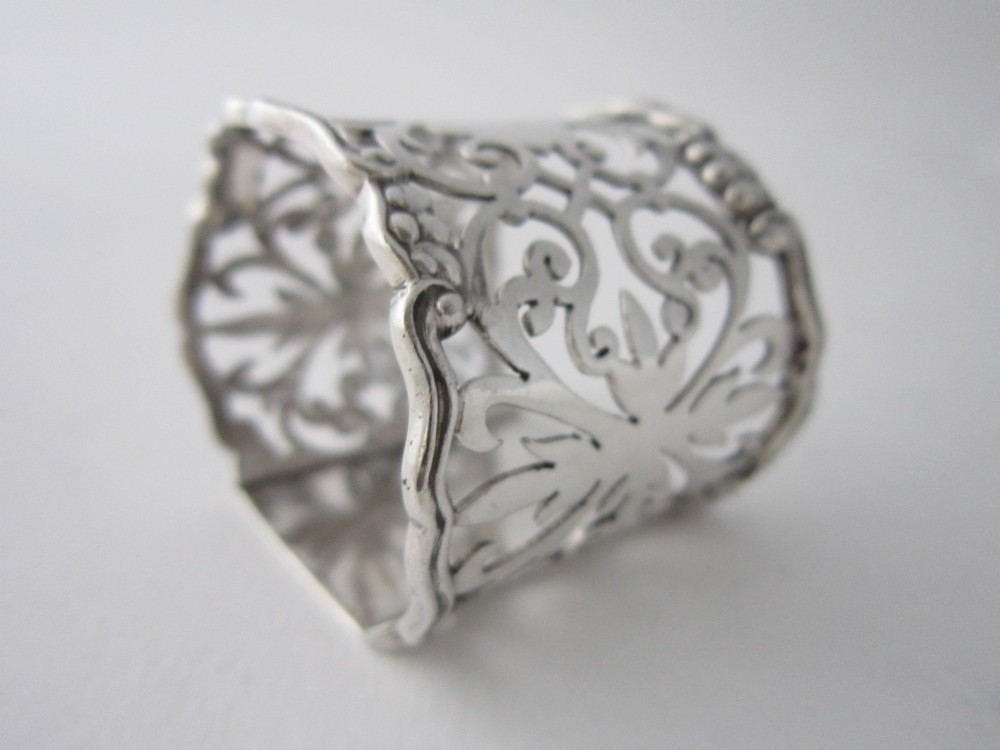 An antique George V sterling silver napkin ring featuring intricate pierced scrollwork and a blank central cartouche. View V
