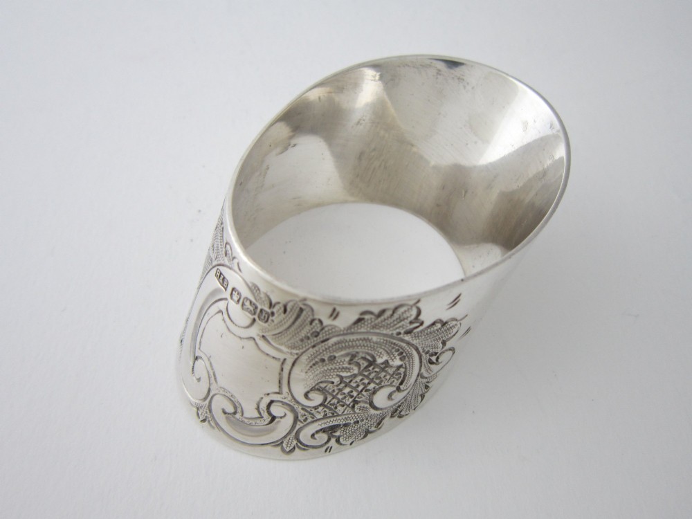 A Victorian sterling silver napkin ring featuring intricate foliate scroll engraving and visible British hallmarks on a reflective curved surface.