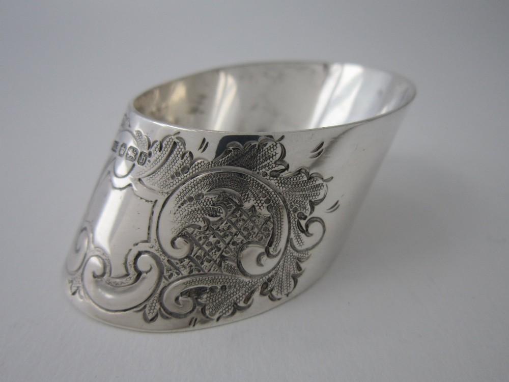 A Victorian sterling silver napkin ring featuring intricate foliate scroll engraving and visible British hallmarks on a reflective curved surface. View II