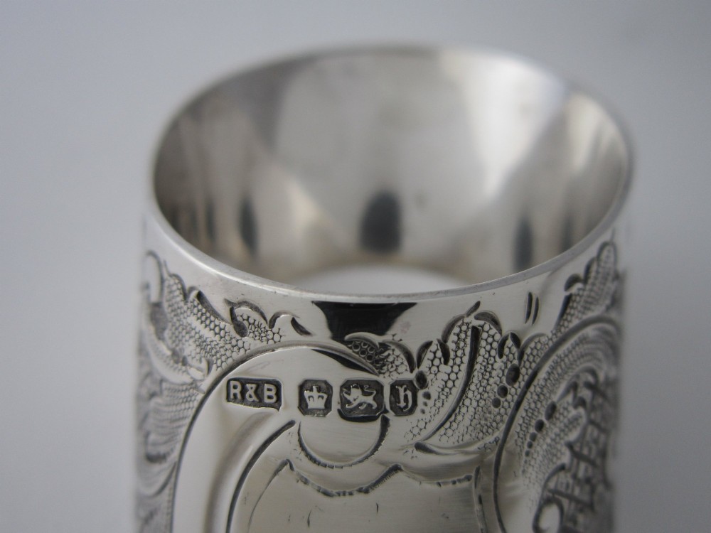 A Victorian sterling silver napkin ring featuring intricate foliate scroll engraving and visible British hallmarks on a reflective curved surface. View V
