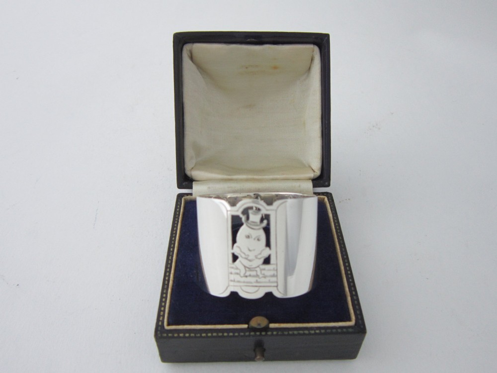 A sterling silver napkin ring featuring a pierced cutout motif of Humpty Dumpty wearing a top hat.