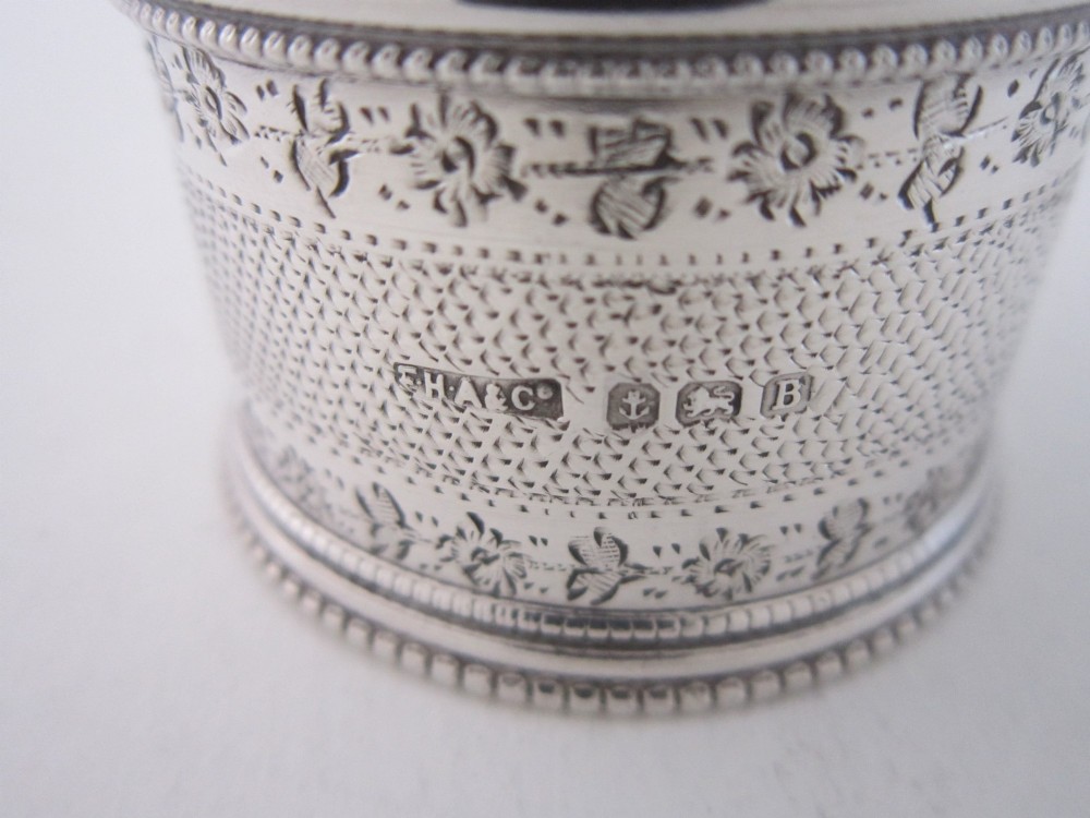 An antique sterling silver napkin ring featuring intricate bright-cut floral engraving, engine-turned lattice patterning, a central cartouche, and beaded borders. View V